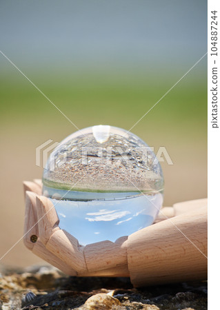 Scenery of mannequin doll one hand and clear crystal glass ball on the beach of the sea Scenery of mannequin doll one hand and clear crystal glass ball on the beach of the sea 104887244