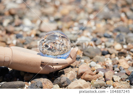 Scenery of mannequin doll one hand and clear crystal glass ball on the beach of the sea 104887245