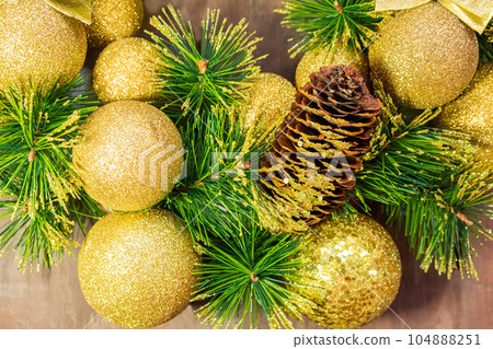 Shiny yellow Christmas balls and cone with barks and pine branches on wooden background. New year card 104888251