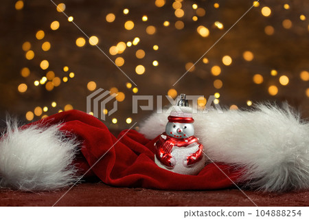 Snowman and red santa claus hat with new year lights in the back. Blurred background. Christmas card 104888254