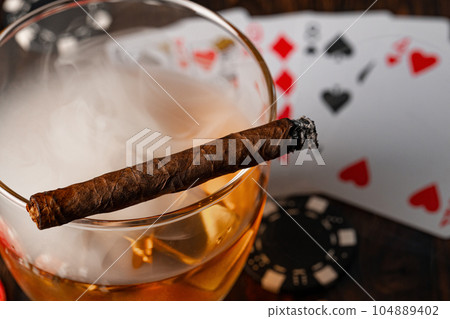 Cuban cigar, whiskey glass and chips on table Cuban cigar, whiskey glass and chips on table 104889402