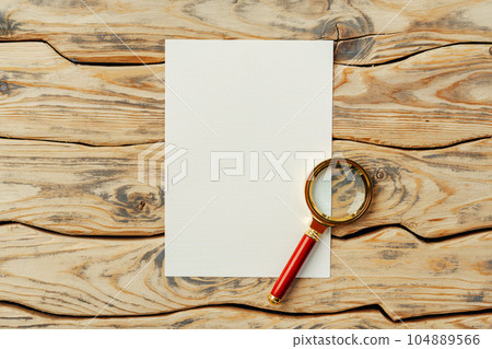 Magnifying glass on old paper on dark brown wooden backgorund 104889566