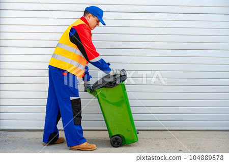 Janitor takes garbage out of trash container outdoors Janitor takes garbage out of trash container outdoors 104889878