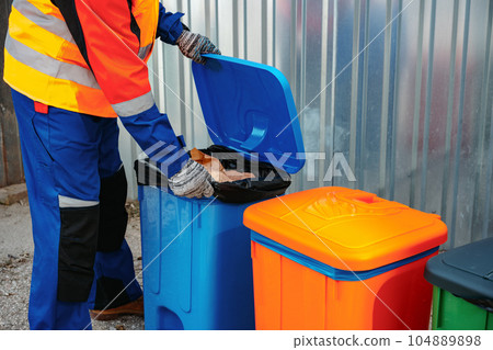 Male janitor in uniform cleans a trash can in the street 104889898