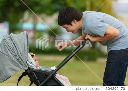 happy father talking and playing with her infant baby in the stroller while resting in park 104890470