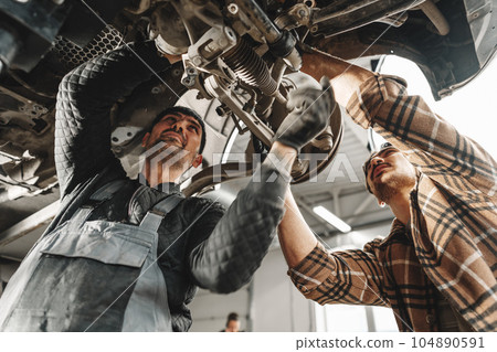 Two male mechanics repairing car in car service Two male mechanics repairing car in car service 104890591