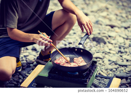 A man grilling pork at a camp gas stove 104890652