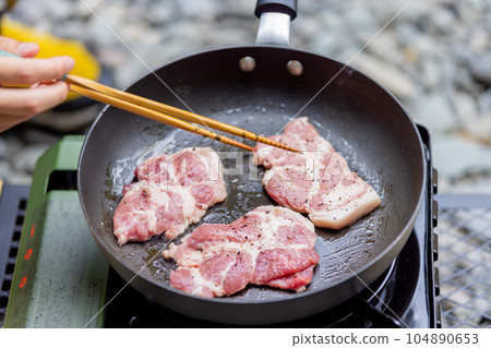 A man grilling pork at a camp gas stove 104890653