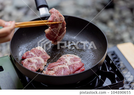 A man grilling pork at a camp gas stove 104890655