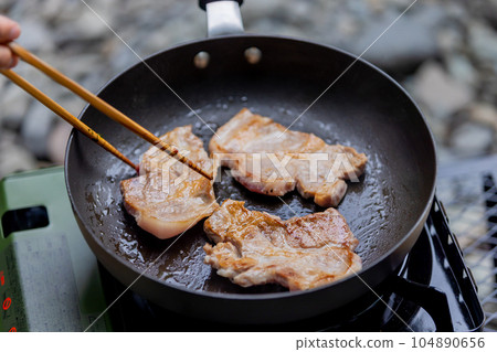 A man grilling pork at a camp gas stove 104890656