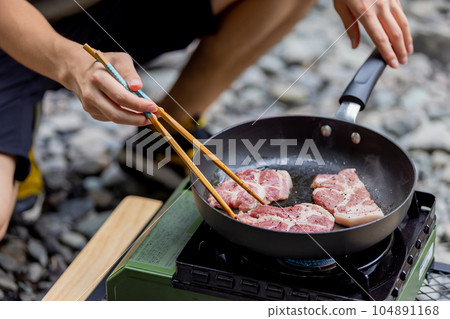 A man grilling pork at a camp gas stove 104891168