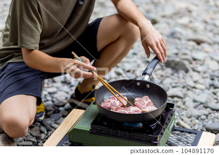 A man grilling pork at a camp gas stove 104891170