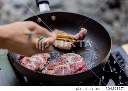 A man grilling pork at a camp gas stove 104891171