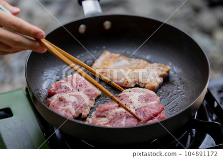 A man grilling pork at a camp gas stove 104891172
