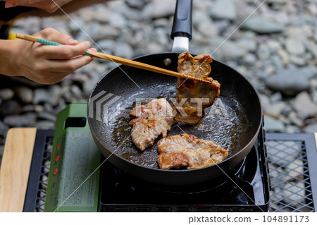 A man grilling pork at a camp gas stove 104891173