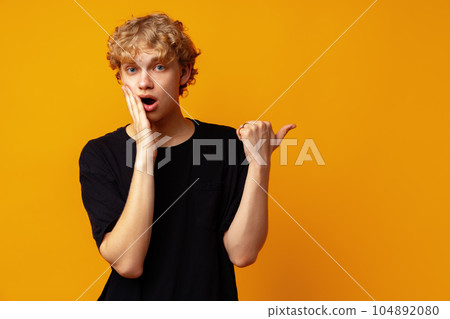 Handsome young man pointing finger to copy space on yellow banner background Handsome young man pointing finger to copy space on yellow banner background 104892080