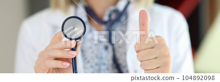 Cropped view of female doctor holding stethoscope and showing thumbs up. 104892098