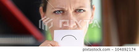 Depressed woman hides her mouth with white paper with sad sign. Depressed woman hides her mouth with white paper with sad sign. 104892174