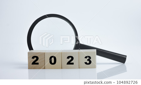 2023 wood block with magnifying glass on white background. 2023 wood block with magnifying glass on white background. 104892726