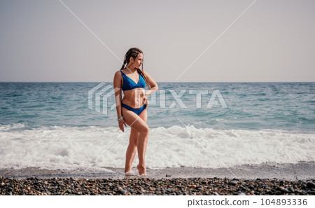 A tourist woman in blue bikini on beach enjoys the turquoise sea during her summer holiday. Rear view. Beach vacation. woman with braids dreadlocks standing with her arms raised enjoying beach ocean. A tourist woman in blue bikini on beach enjoys the turquoise sea during her summer holiday. Rear view. Beach vacation. woman with braids dreadlocks standing with her arms raised enjoying beach ocean. 104893336