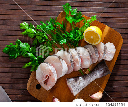 Raw hake sliced on cutting board Raw hake sliced on cutting board 104893364