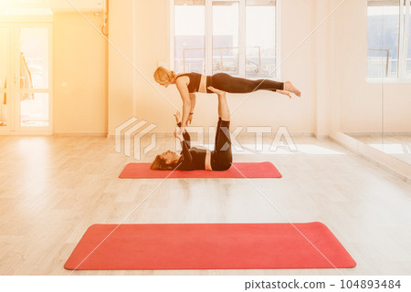 Well looking middle aged woman with black hair, fitness instructor in leggings and tops doing stretching and pilates on yoga mat near the mirror. Female fitness yoga routine concept. Healthy lifestyle 104893484