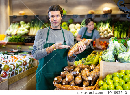Male salesman near fruit and vegetables stalls offering to buy yuca 104893540