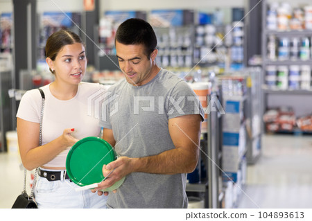 Interested couple talking and selecting paints in building supplies store 104893613