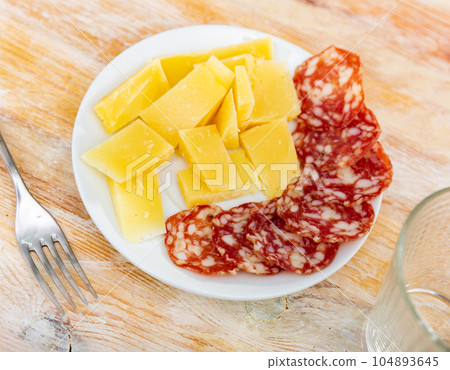 Plate of sliced sausage and cheese on table Plate of sliced sausage and cheese on table 104893645