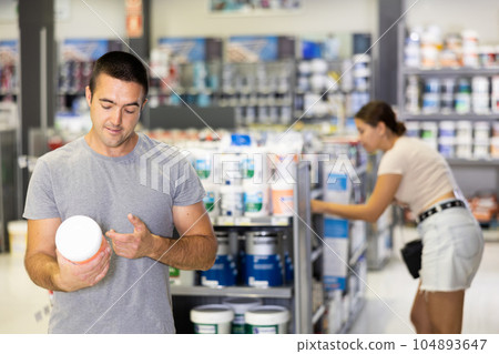 Interested man reading labels on paint cans in hardware store Interested man reading labels on paint cans in hardware store 104893647