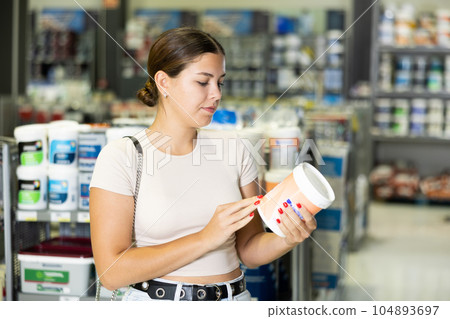 Woman buys paint tin in paintwork material store for carrying out internal finishing work on object 104893697