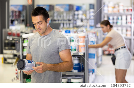 Man buys tin with paint in paintwork material store for carrying out internal finishing work on object Man buys tin with paint in paintwork material store for carrying out internal finishing work on object 104893752