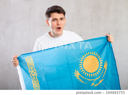 Male fan in casual clothes holds canvas of national Kazakh flag in hands and chants popular slogan Male fan in casual clothes holds canvas of national Kazakh flag in hands and chants popular slogan 104893755