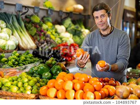 Man diligently picking out mandarin orange to buy in vegetable aisle of supermarket Man diligently picking out mandarin orange to buy in vegetable aisle of supermarket 104893767