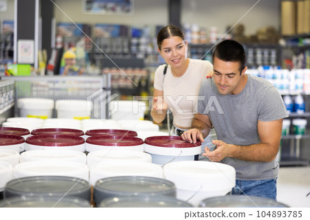 Interested couple talking and selecting paints in building supplies store 104893785
