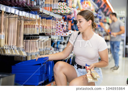 Woman buy brushes and tray expendable materials in paint department of construction store. 104893864