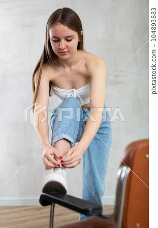 Young woman tying shoelaces with foot on chair 104893883