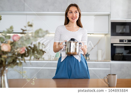 Smiling middle-aged woman holding hot pan in the kitchen Smiling middle-aged woman holding hot pan in the kitchen 104893884