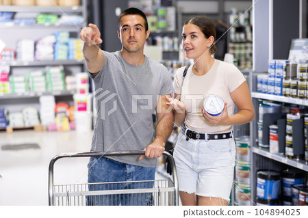 Positive couple talking while choosing paints and tools in store Positive couple talking while choosing paints and tools in store 104894025