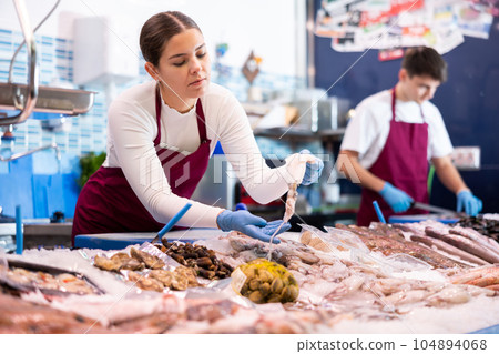 Positive saleswoman demonstrating calamary in fish store Positive saleswoman demonstrating calamary in fish store 104894068