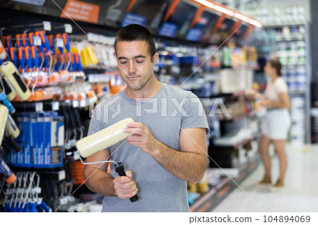Man buying tools for house decoration in paint supplies store - paint roller Man buying tools for house decoration in paint supplies store - paint roller 104894069