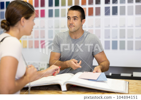 Male salesman of paintwork material shop advises woman buyer with samples and product catalog 104894151
