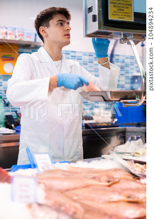 Proficient salesman weighing scaldfish on balance in fish store 104894234