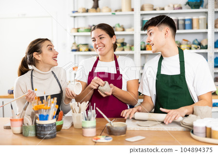 Two young women and young man making pottery 104894375