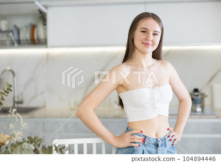 Portrait of long-haired young woman standing in kitchen 104894446