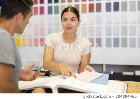 Female saleswoman of paintwork material shop advises man buyer with samples and product catalog Female saleswoman of paintwork material shop advises man buyer with samples and product catalog 104894466