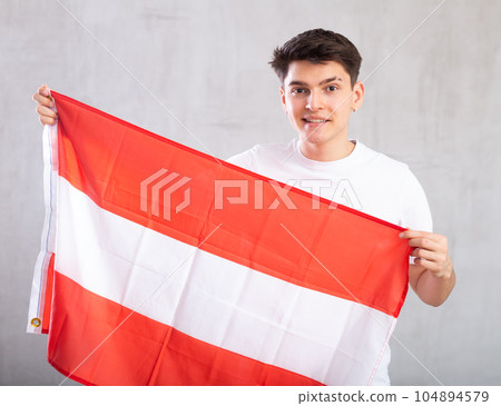 Reliant positive young man holds big national flag of Austria with confident smile showing teeth 104894579