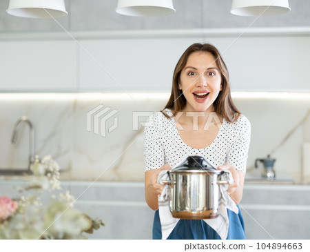 Smiling middle-aged woman holding hot pan in the kitchen Smiling middle-aged woman holding hot pan in the kitchen 104894663