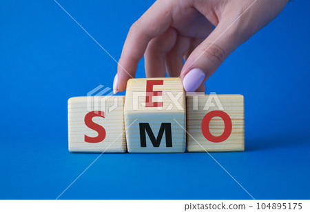 SEO vs SMO symbol. Businessman hand turns wooden cubes and changes the word SMO to SEO. Beautiful blue background. SEO vs SMO and business concept. Copy space SEO vs SMO symbol. Businessman hand turns wooden cubes and changes the word SMO to SEO. Beautiful blue background. SEO vs SMO and business concept. Copy space 104895175