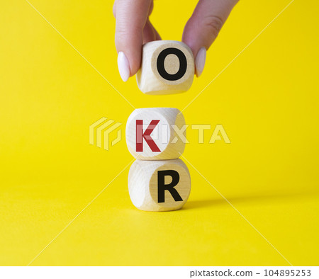 OKR objectives and key results symbol. Wooden cubes with words OKR objectives and key results. Businessman hand. Beautiful yellow background. Business and OKR concept. Copy space. 104895253